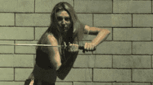 a woman is standing in front of a brick wall holding a sword .