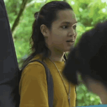 a young man with long hair and a yellow shirt is standing next to a woman and talking to her .