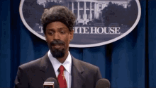 a man in a suit and tie is standing in front of a microphone in front of a white house sign .