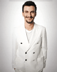 a man in a white suit has his hands in his pockets and is smiling