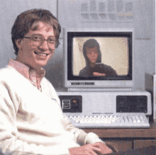 bill gates is smiling while sitting in front of a computer monitor