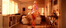 a woman in a pink shirt is dancing in a room with a bed in the background