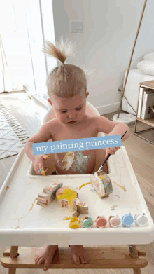 a baby is sitting in a high chair painting with a sign that says my painting princess