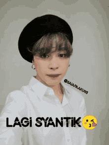 a person wearing a black beret and a white shirt with the words lagi syanik on the bottom