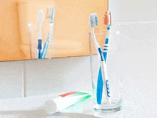 two toothbrushes and a tube of toothpaste in a glass on a bathroom sink .