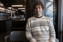 a man wearing a striped sweater sits in a chair in front of a restaurant