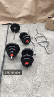 a set of dumbbells and barbells are sitting on a concrete surface with a sign that says enidservice above them