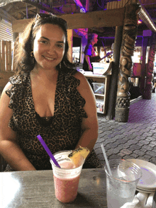 a woman in a leopard print dress sits at a table with a drink and a purple straw