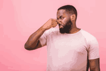 a man with a beard is covering his nose with his hand against a pink background