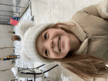 a little girl wearing a white hat and a tan jacket is smiling