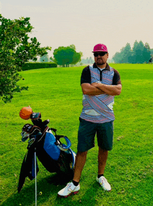 a man with his arms crossed stands in front of a golf bag