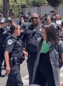 a group of police officers are walking down a street with a woman wearing a green scarf around her neck .