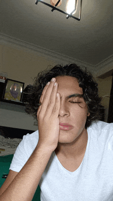 a young man in a white shirt covering his face with his hand