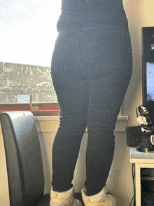 a woman wearing black jeans and white nike shoes stands in front of a computer monitor