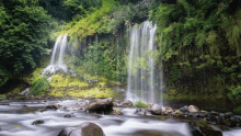 a waterfall is surrounded by greenery and rocks