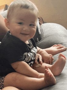 a baby is sitting on a couch wearing a black shirt that says skulls