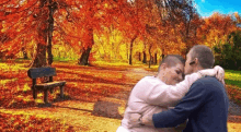 a man and a woman are hugging in front of a park bench covered in autumn leaves .