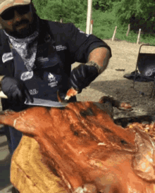 a man is cutting up a pig with a knife while wearing an apron that says ' flame ' on it