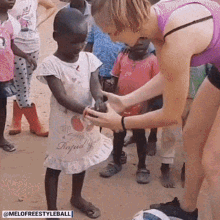 a woman in a purple tank top is holding a small child 's hand in front of a group of children