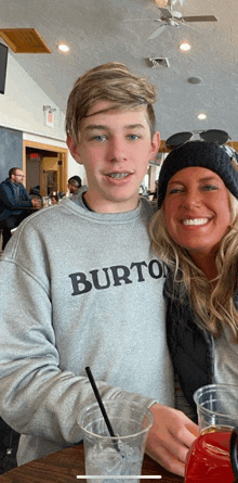 a boy wearing a burton sweatshirt stands next to a smiling woman