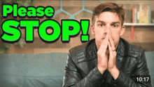a man in a leather jacket is covering his mouth with his hands in front of a green sign that says please stop