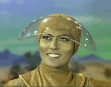 a woman in a gold costume is smiling and wearing a clear helmet on her head .