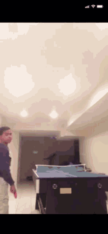 a man playing ping pong in a basement with a cell phone in the background