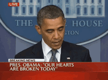 a man in a suit and tie stands in front of a sign that says breaking news pres obama our hearts are broken today