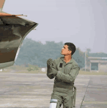 a man in a military uniform is standing on a runway looking at a plane .