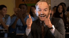 a man in a suit and tie is giving a thumbs up in front of a group of people .