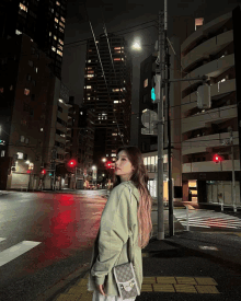 a woman in a green sweatshirt is standing in front of a street at night