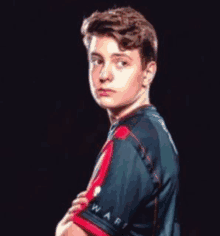 a young man in a blue and red shirt is standing with his hands folded .