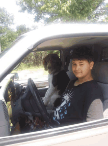 a boy is sitting in the driver 's seat of a car with a dog behind him