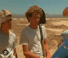 a young man is holding a shovel in the desert while standing next to another young man .