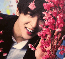 a young man is smiling behind a bunch of pink flowers ..