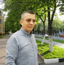 a man in a blue and white plaid shirt is standing on a sidewalk