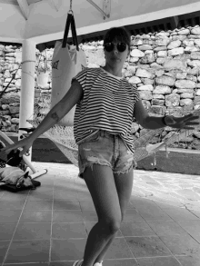 a woman in a striped shirt is dancing in front of an everlast punching bag