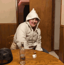 a man wearing a hoodie sits at a table with a bottle of crown royal