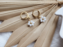 a pair of gold hoop earrings with white beads on a dried palm leaf