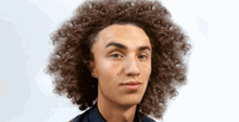 a young man with long curly hair is looking at the camera .
