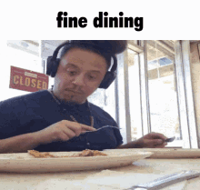 a man wearing headphones is sitting at a table with a plate of food and a sign that says closed