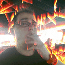 a man wearing glasses is smoking a cigarette in front of flames coming out of the ceiling .