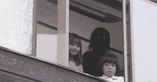 a group of children are looking out of a window with a silhouette of a person behind them .