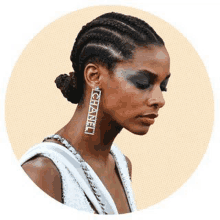 a woman with braids and chanel earrings is wearing a white dress .