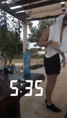 a woman is standing in front of a table with the time 5:35