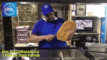 a man in a blue shirt is cutting a loaf of bread in front of a sign that says " erol "