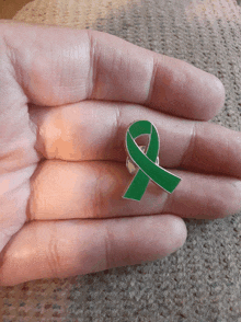 a person is holding a green ribbon pin on their finger