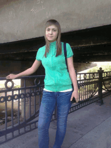 a woman in a green shirt stands in front of a bridge