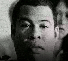 a black and white photo of a man 's face with a woman 's face in the background .