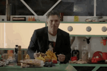 a man in a suit is eating french fries in a kitchen with a bottle of coca cola in the background